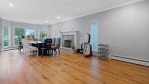 A spacious dining area with a wooden floor, a dining table with chairs, a fireplace, and large windows. - VANCOUVER WEST BEAUTIFUL HOUSE (Vancouver)