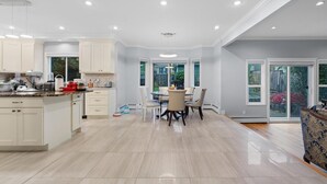 A modern kitchen with white cabinets, a dining area with a table and chairs, and large windows. - VANCOUVER WEST BEAUTIFUL HOUSE (Vancouver)