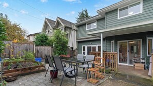 A patio area with a table and chairs, a wooden deck, and a house in the background. - VANCOUVER WEST BEAUTIFUL HOUSE (Vancouver)