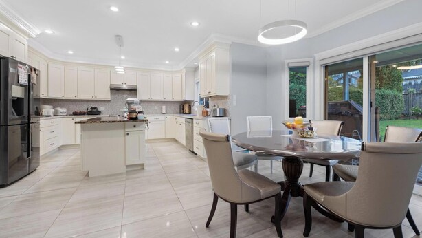 A modern kitchen with white cabinets, a central island, and a dining area with a glass table and chairs. - VANCOUVER WEST BEAUTIFUL HOUSE (Vancouver)