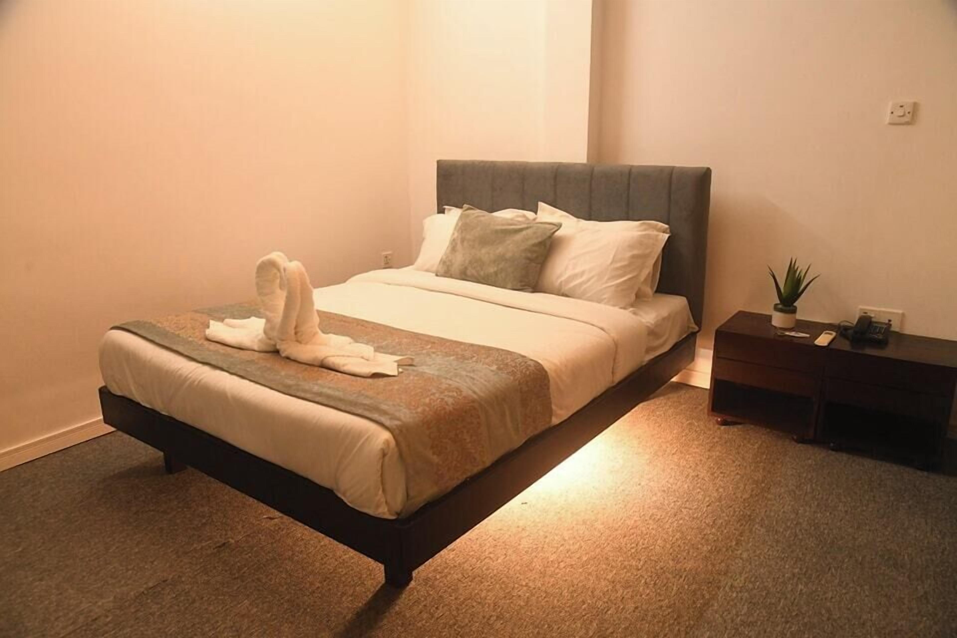 A neatly made bed with a grey headboard, a bedside table with a plant, and a wall socket.