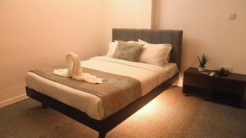 A neatly made bed with a grey headboard, a bedside table with a plant, and a wall socket.