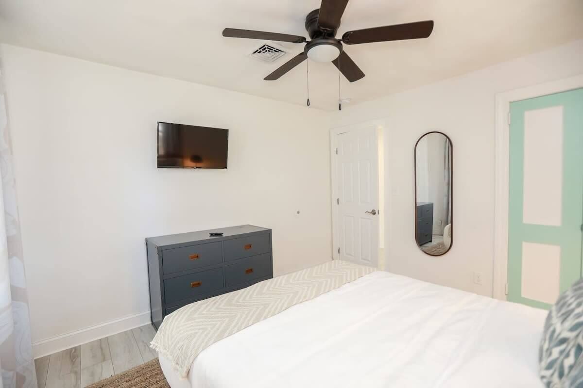 Ein Schlafzimmer mit Bett, Kommode, Deckenventilator, Fernseher und einer Tür.