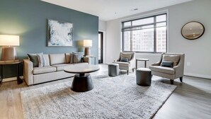A modern living room with a sofa, armchairs, a coffee table, and a large window providing a view of the city. - Sojourn | Courtland Towers w/ Entertainment Area (Arlington)