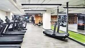 A gym with multiple treadmills, weight machines, and a TV screen in the background. - Sojourn | Courtland Towers w/ Entertainment Area (Arlington)