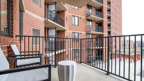 Un balcone con tavolo e sedie bianche, un edificio in mattoni con balconi e vista sui dintorni.