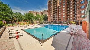 Una piscina con lettini e un pergolato, circondata da un edificio in mattoni e vegetazione.