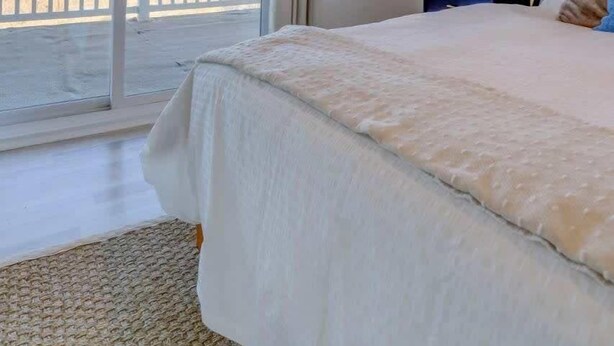 Quarto com uma cama grande, ventoinha no teto, janela com vista para a praia e mesa de cabeceira com luminária.