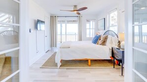Quarto com cama, ventilador de teto, mesa de cabeceira e vista para o exterior.