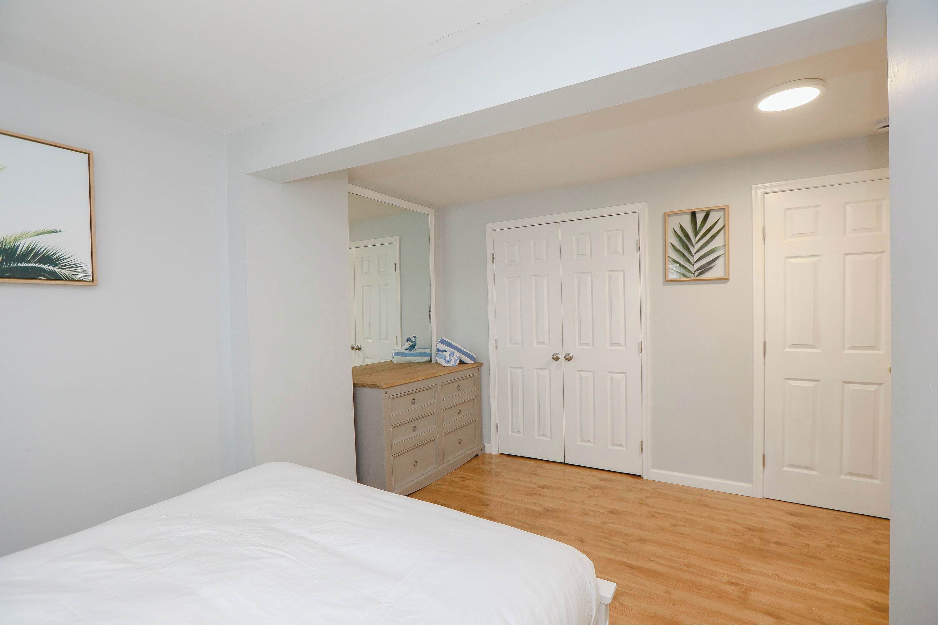 Une chambre à coucher avec un lit, une commode, un miroir et deux portes blanches.