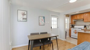 A modern kitchen with wooden cabinets, a white stove, and a dining area with a table and chairs. - Sojourn Willoughby Spit Chic Shack <1min. to Beach (Norfolk)