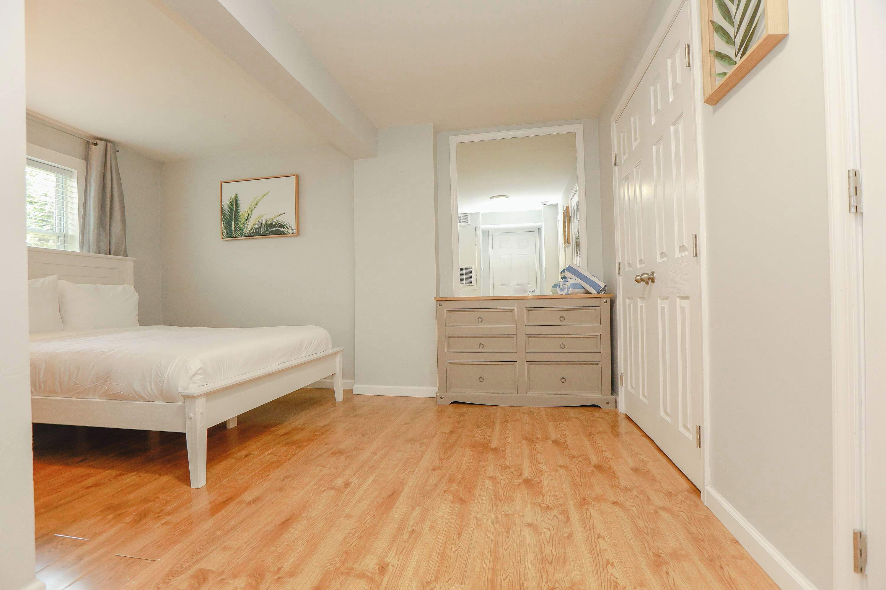 A bedroom with a bed, a dresser, a mirror, and a door.
