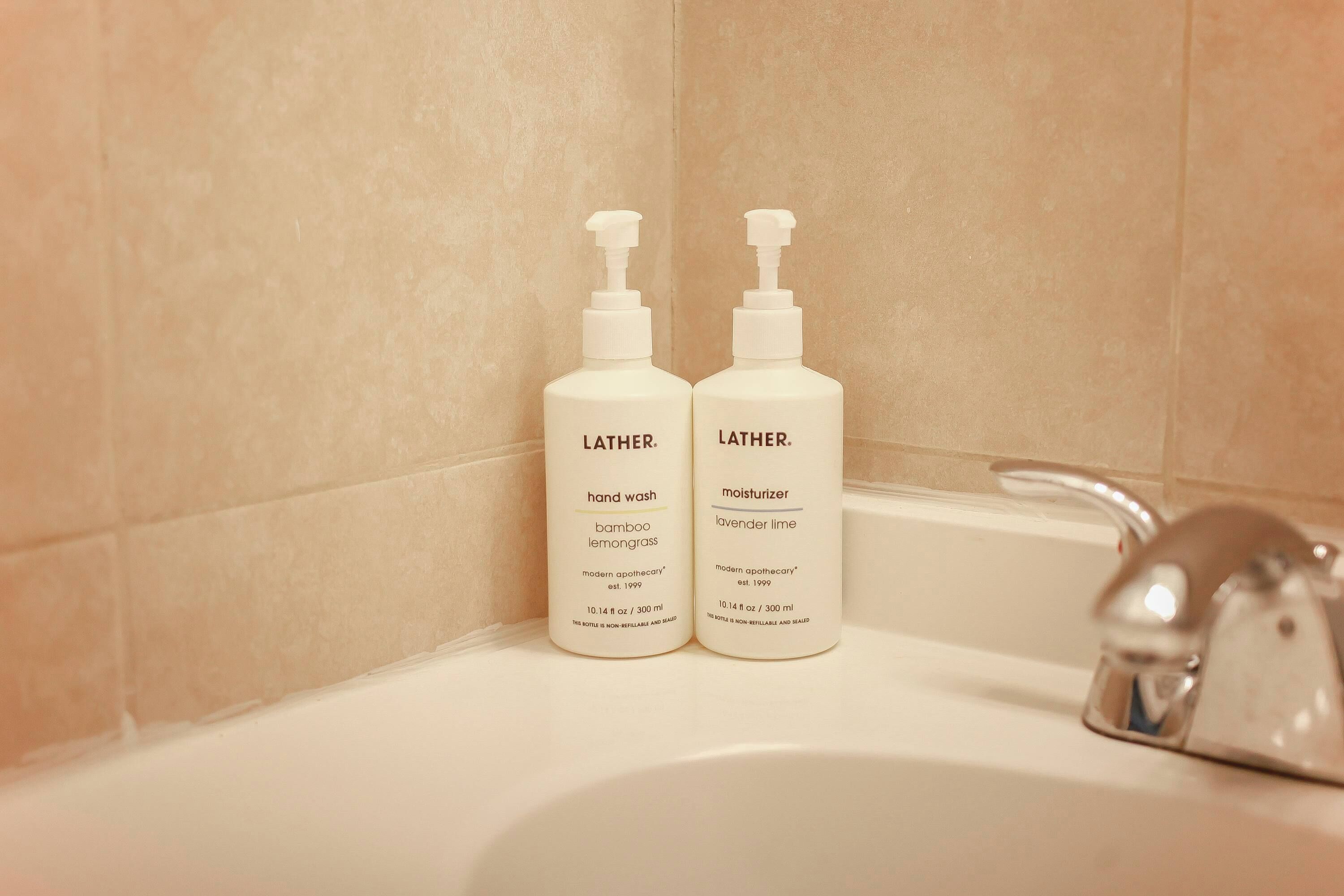 Dos amples de sabó líquid i crema hidratant sobre un lavabo de bany.