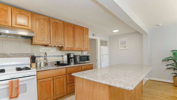 A kitchen with wooden cabinets, a granite countertop, a stove, a microwave, and a refrigerator. - Sojourn Willoughby Spit Chic Shack <1min. to Beach (Norfolk)