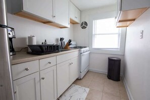 Eine kompakte Küche mit weißen Schränken, einem eingebauten Ofen, einer Kaffeemaschine und einem Fenster, das für natürliches Licht sorgt.