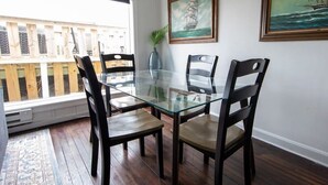 Zona pranzo con tavolo in vetro e quattro sedie, un pontile in legno all'esterno e due quadri appesi al muro.