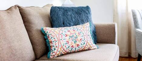 Un sofá color beige con un cojín estampado y una manta azul.