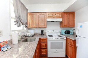 A kitchen with wooden cabinets, a white stove, a microwave, and granite countertops. - Sojourn | Ocean Hideaway unit 3 | 2 Bedroom (Norfolk)