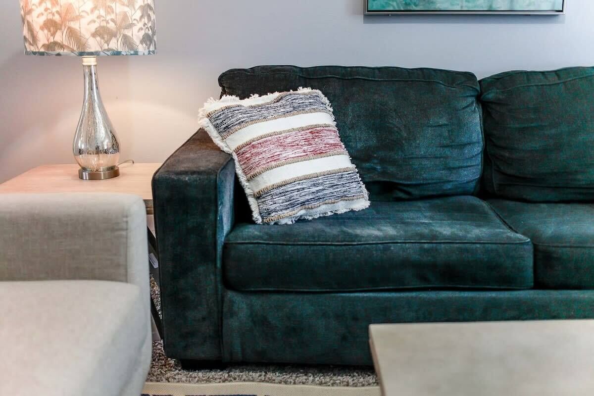 A dark green sofa with a striped throw pillow, a lamp with a floral shade, and a framed picture on the wall.