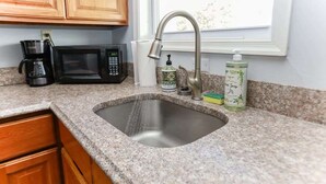 Eine Küche mit Granit-Arbeitsplatten, einer Edelstahl-Spüle, einer Kaffeemaschine, einer Mikrowelle und einem Fenster über der Spüle.