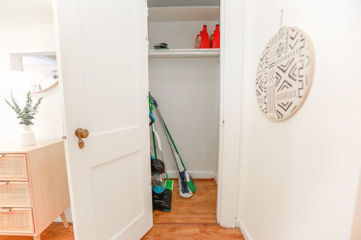Puerta blanca que da a un área de almacenamiento con productos de limpieza y un trapeador.
