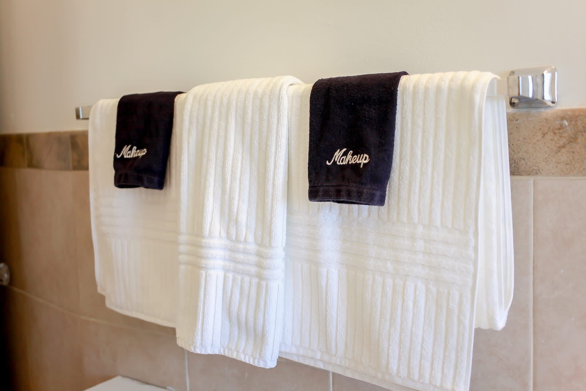 Deux serviettes blanches et des serviettes noires sont suspendues sur un porte-serviettes dans une salle de bain.