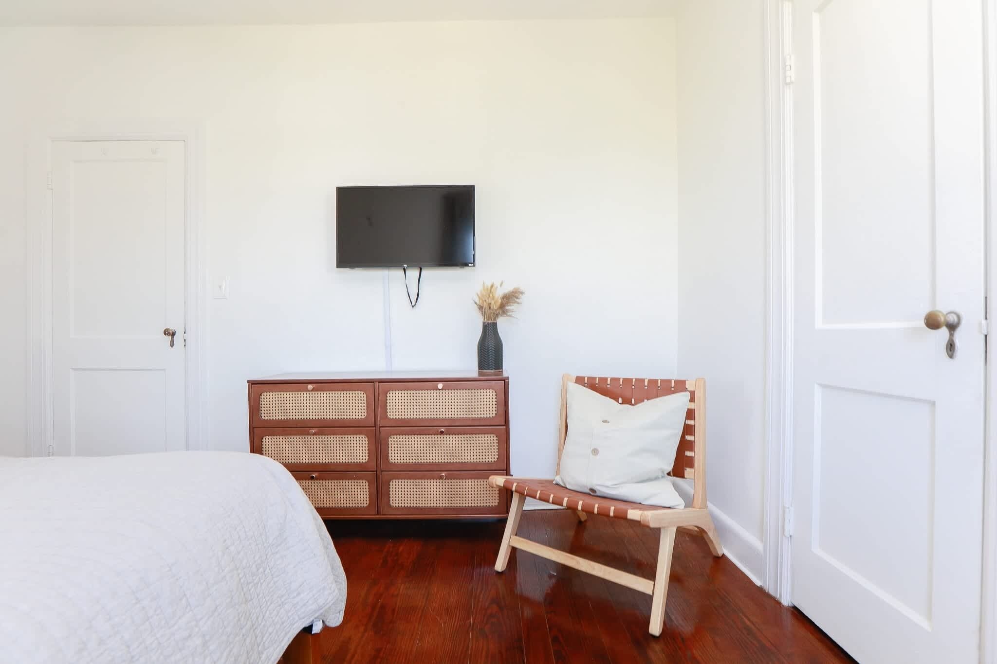 A bedroom with a bed, a wooden dresser, a television, and a door.