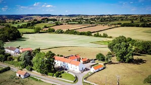 Vista aérea de uma zona rural com um grande edifício branco e telhado vermelho, rodeado por campos e árvores.
