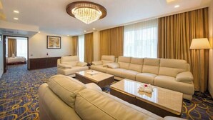 A hotel room with a large beige sofa, two armchairs, a coffee table, and a chandelier. - Grand Palace Sylhet (Sylhet)