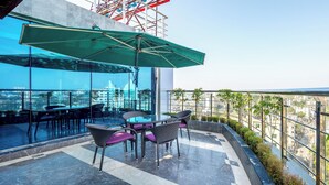 A rooftop terrace with a glass table and chairs, a green umbrella, and a view of the cityscape. - Grand Palace Sylhet (Sylhet)