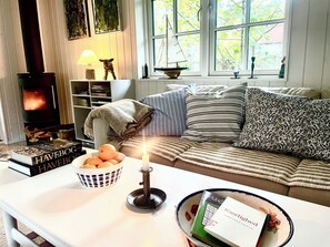 Un salon chaleureux avec une cheminée, un canapé agrémenté de coussins à rayures, une table avec une bougie et un bol rempli d’oranges.