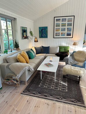 Un salon avec un canapé, une table basse, un tapis à motifs et un mur orné d’un ensemble de photos encadrées.