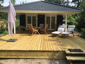 A covered outdoor deck with wooden furniture, including chairs and a table, and a patio umbrella. - Perfect base near beach and shops (Væggerløse)