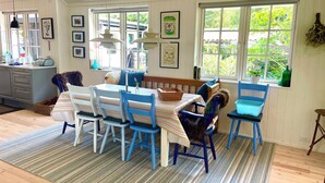 Un coin repas avec une table dressée pour quatre personnes, entourée de chaises, d’un banc et d’une fenêtre donnant sur un paysage verdoyant.