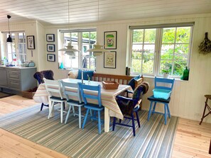 A dining area with a table set for four, surrounded by chairs, a bench, and a window with a view of greenery. - Perfect base near beach and shops (Væggerløse)