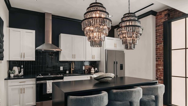 Een moderne keuken met witte kasten, een zwart aanrecht en twee kristallen kroonluchters.