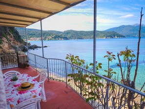 Una terraza con mesa y sillas, con vistas a una zona costera de aguas azules cristalinas y colinas lejanas.