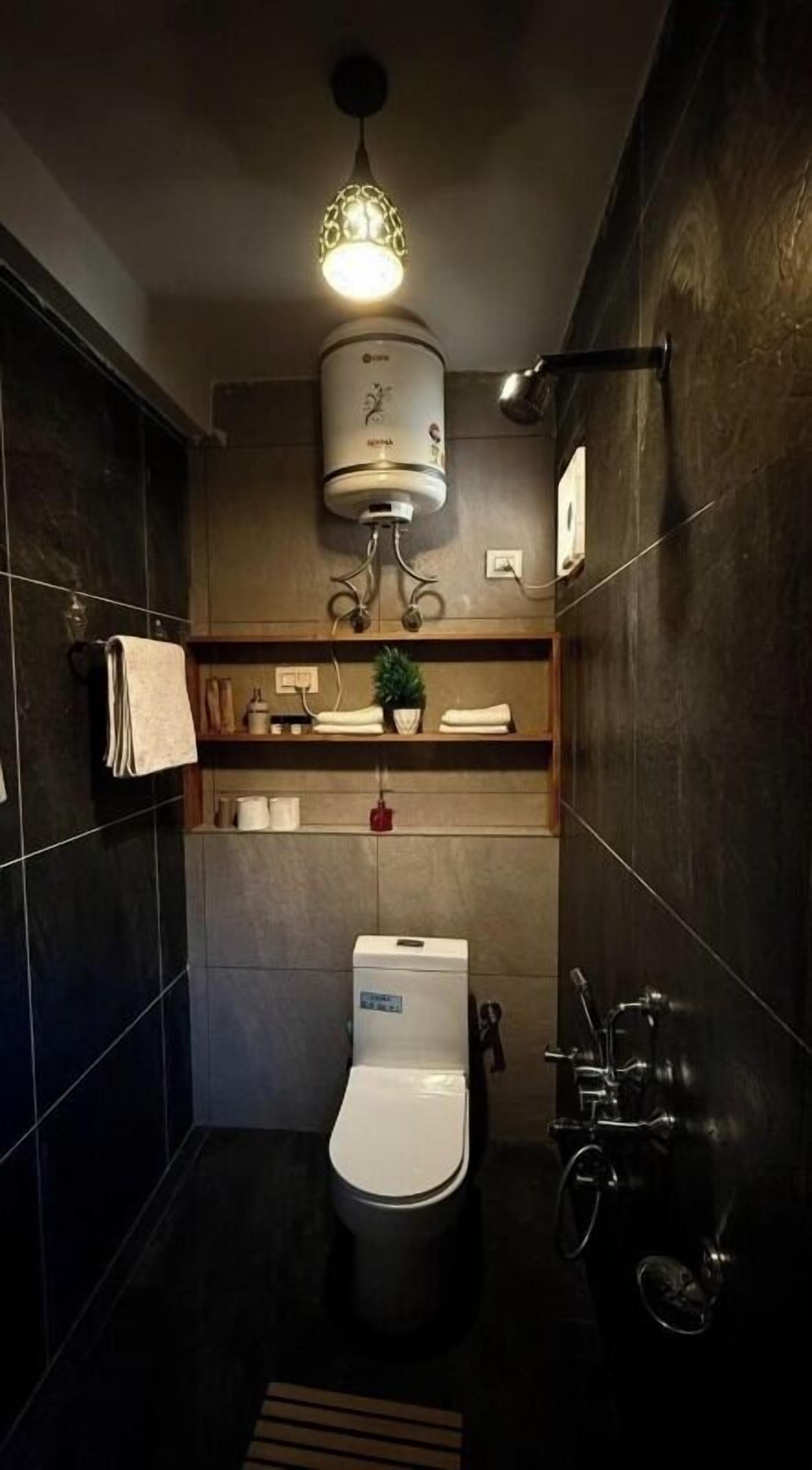 Une salle de bain moderne avec des toilettes, une étagère contenant des articles de toilette et un luminaire suspendu.
