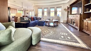 A spacious living room with a sectional sofa, a coffee table, and a large rug. There is a kitchen area with wooden cabinets and a built-in oven. - Upscale 4 bedroom family home near Zion w pool & hot tub (Kanab)