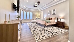 A bedroom with a bed, bedside tables, a ceiling fan, and a large window. - Upscale 4 bedroom family home near Zion w pool & hot tub (Kanab)