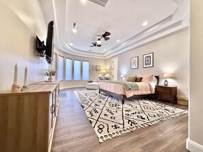 Ein Schlafzimmer mit einem Bett, Nachttischen, einem Deckenventilator und einem großen Fenster.