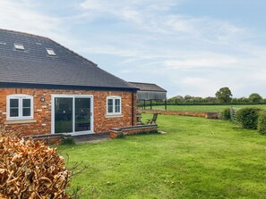 A brick house with a large sliding glass door, a covered patio, and a grassy yard. - Holly Tree Barn - UK49607 (Minshull Vernon, near Nantwich)