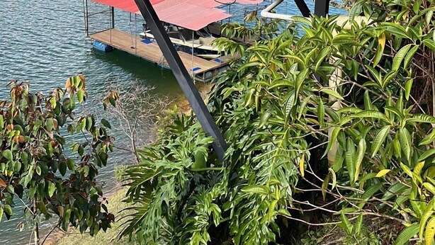 A wooden deck with a red umbrella, overlooking a lake with lush greenery and a clear sky. - Glamping Boreal (Guatapé)