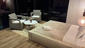 A modern bedroom with a large bed, a small round table with a bottle, and two chairs. - Glamping Boreal (Guatapé)