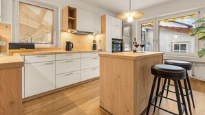Una cocina moderna con armarios blancos, encimera de madera, horno empotrado y una zona de bar con taburetes.