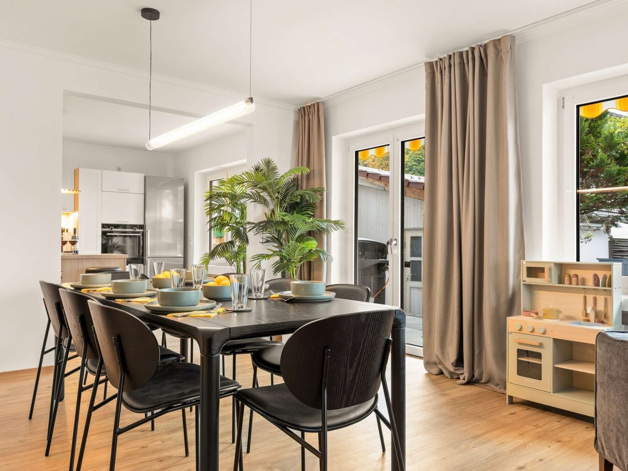 Een moderne eetruimte met een lange tafel, zwarte stoelen en een keuken op de achtergrond.