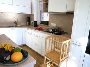 A modern kitchen with white cabinets, a wooden chair, and a fruit bowl on the counter. - Holiday home with terrace whirlpool, families welcome! (Ruhpolding)