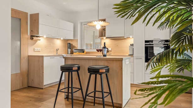 Una cocina moderna con encimera de madera, dos taburetes de bar, una botella de vino y una planta.