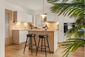Una cocina moderna con encimera de madera, dos taburetes de bar, una botella de vino y una planta.