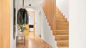 Un intérieur moderne avec un escalier en bois, un couloir agrémenté d’une plante et un porte-manteau.